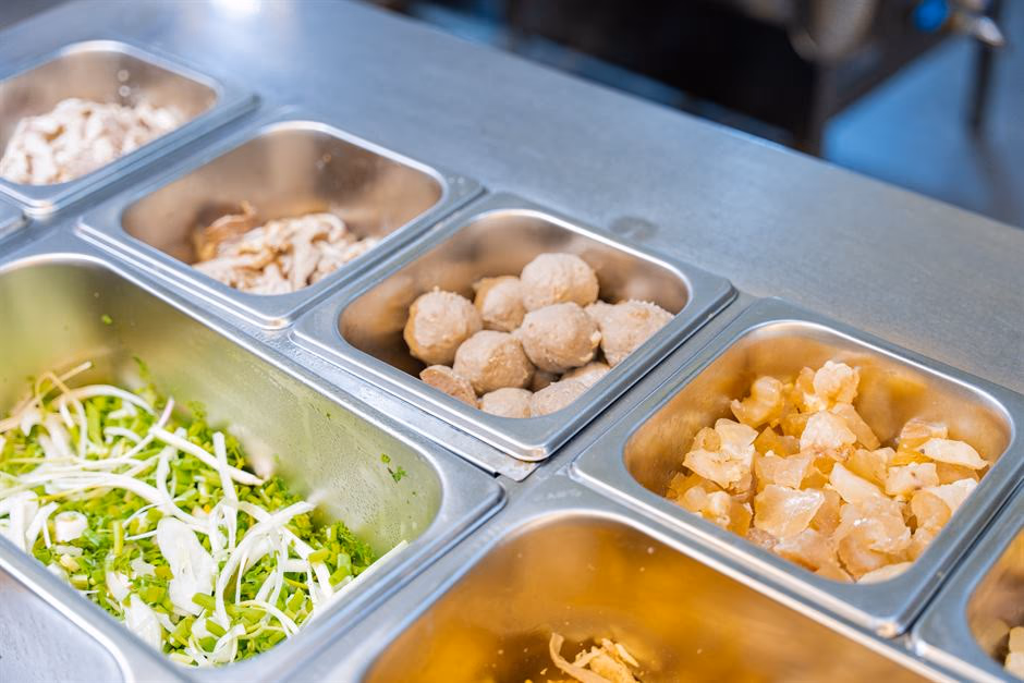 Khu bếp sơ chế của Phở ’S với các khay nguyên liệu xếp dọc mặt bàn thép.